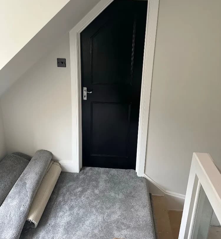 Black internal door fitted with white frame on a sloped-ceiling landing, carpet being laid