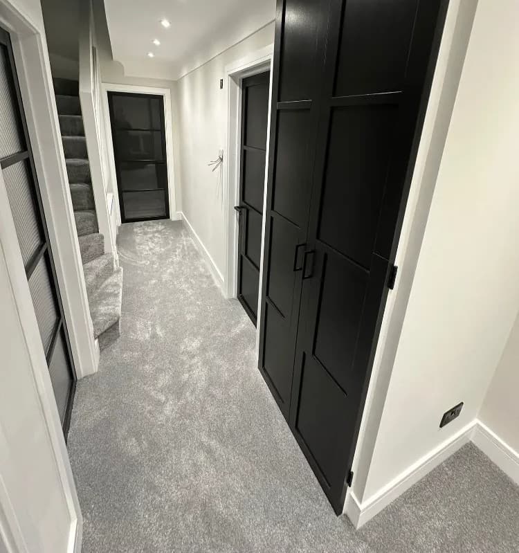 Black panelled fitted cupboard doors in a hallway with grey carpet and staircase