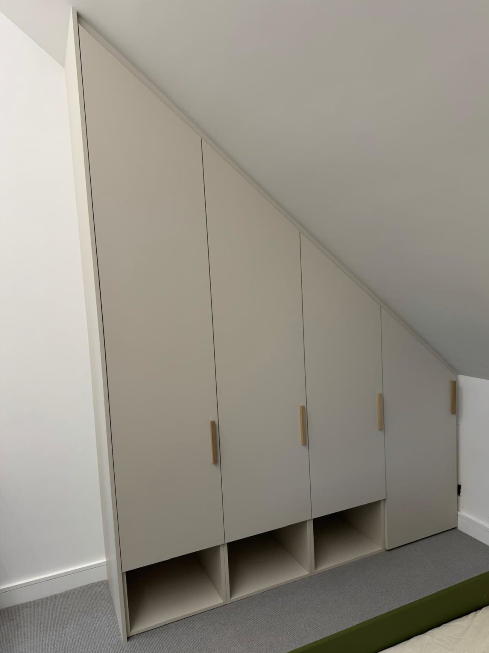 Fitted wardrobe built to a sloped loft ceiling, with oak handles and open shoe cubbies