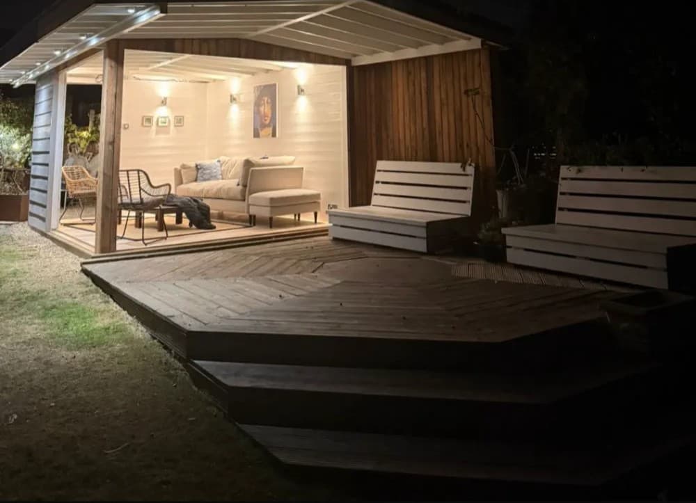 Timber-clad garden studio with lit interior and multi-tier octagonal deck at night