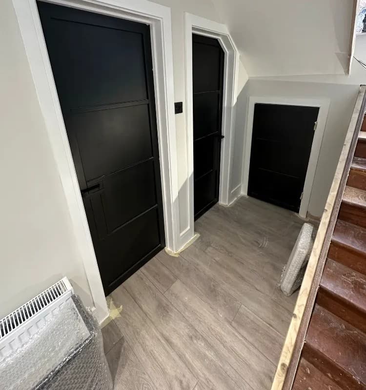 Black panelled internal doors with white frames on a landing with grey wood-effect flooring