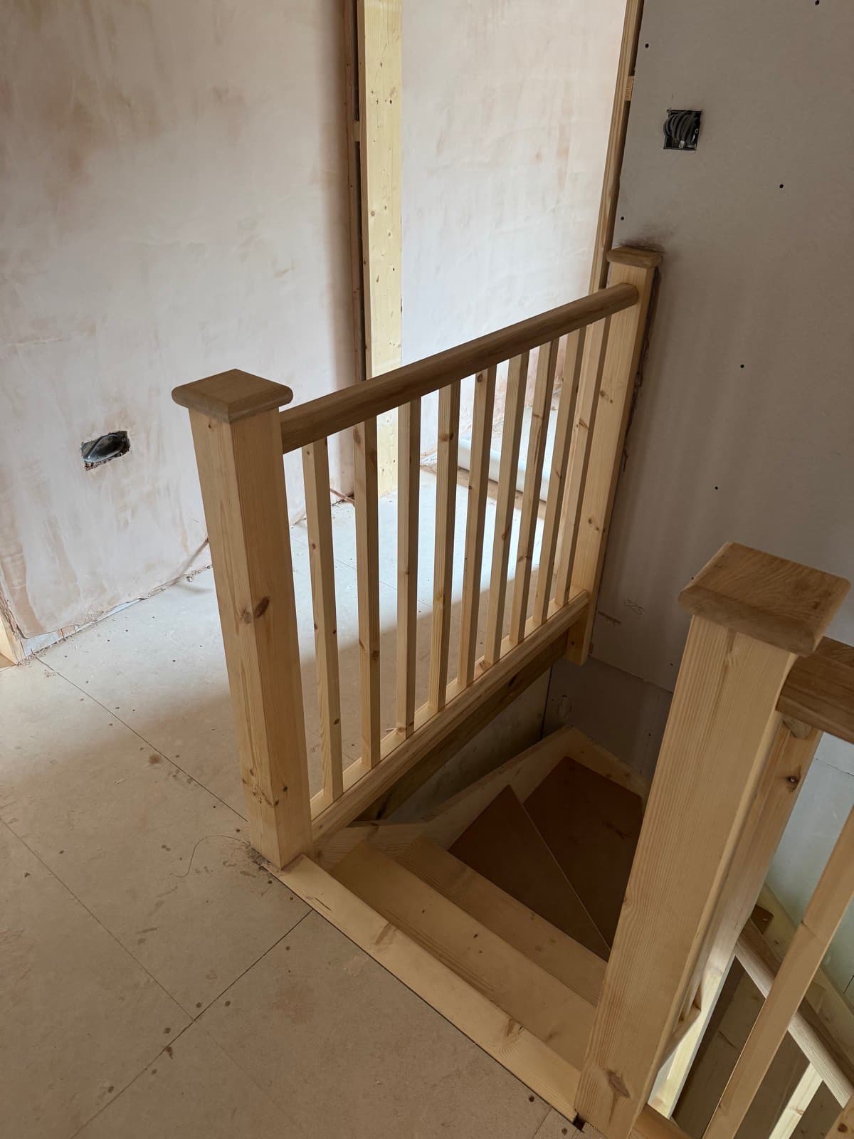 Newly fitted pine staircase with spindle balustrade at a landing, walls unfinished
