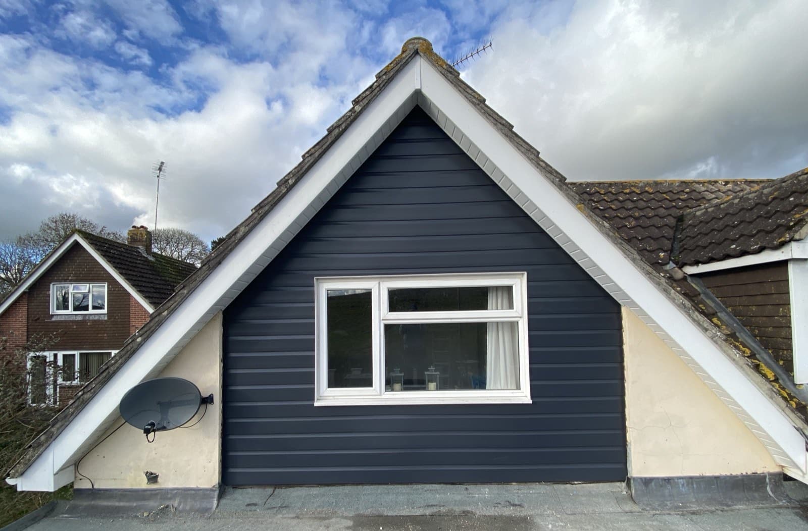 Dark grey weatherboard cladding on a gable end with white trim and a central window