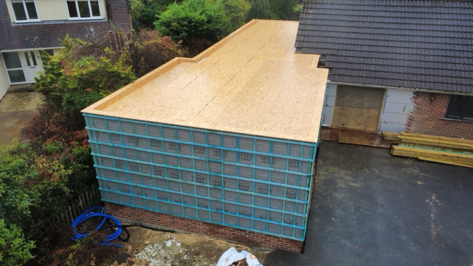 Aerial view of a timber frame extension mid-build with OSB roof deck and stud walls