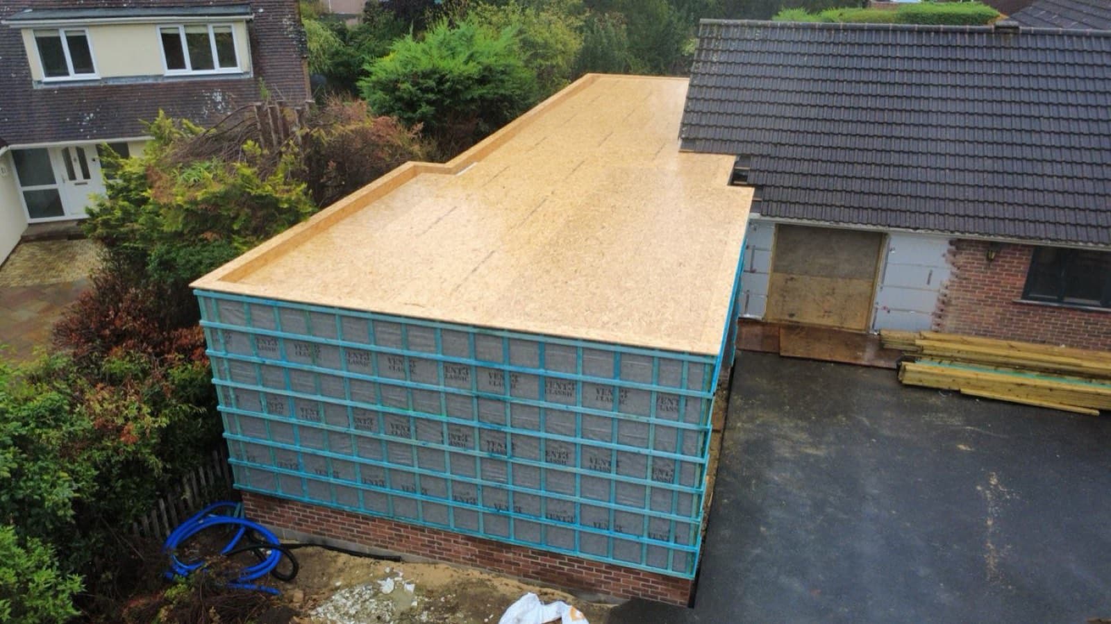 Aerial view of a timber-frame extension roof deck and wall panels mid-build